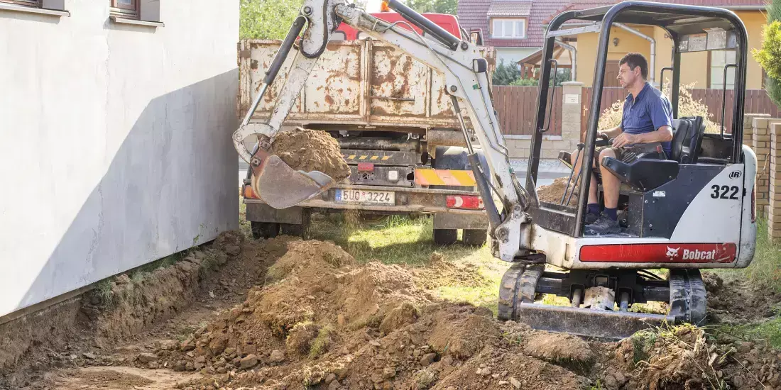 A man in a JCB digging up the ground beside a house